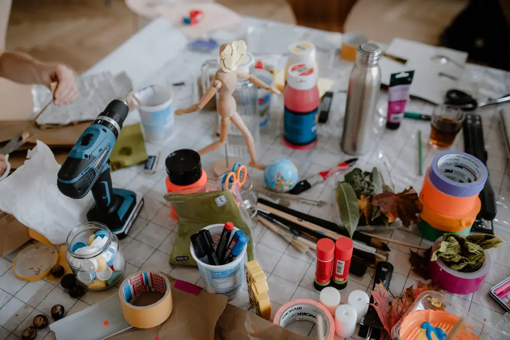 Foto eines Tisches während eines Kunstworkshops. Auf dem Tisch stehen verschiedene Materialien wie Klebebänder, Farben, Pinsel, Stifte, ein Akku-Bohrer sowie verschiedene Naturelemente wie Blätter und Äste.